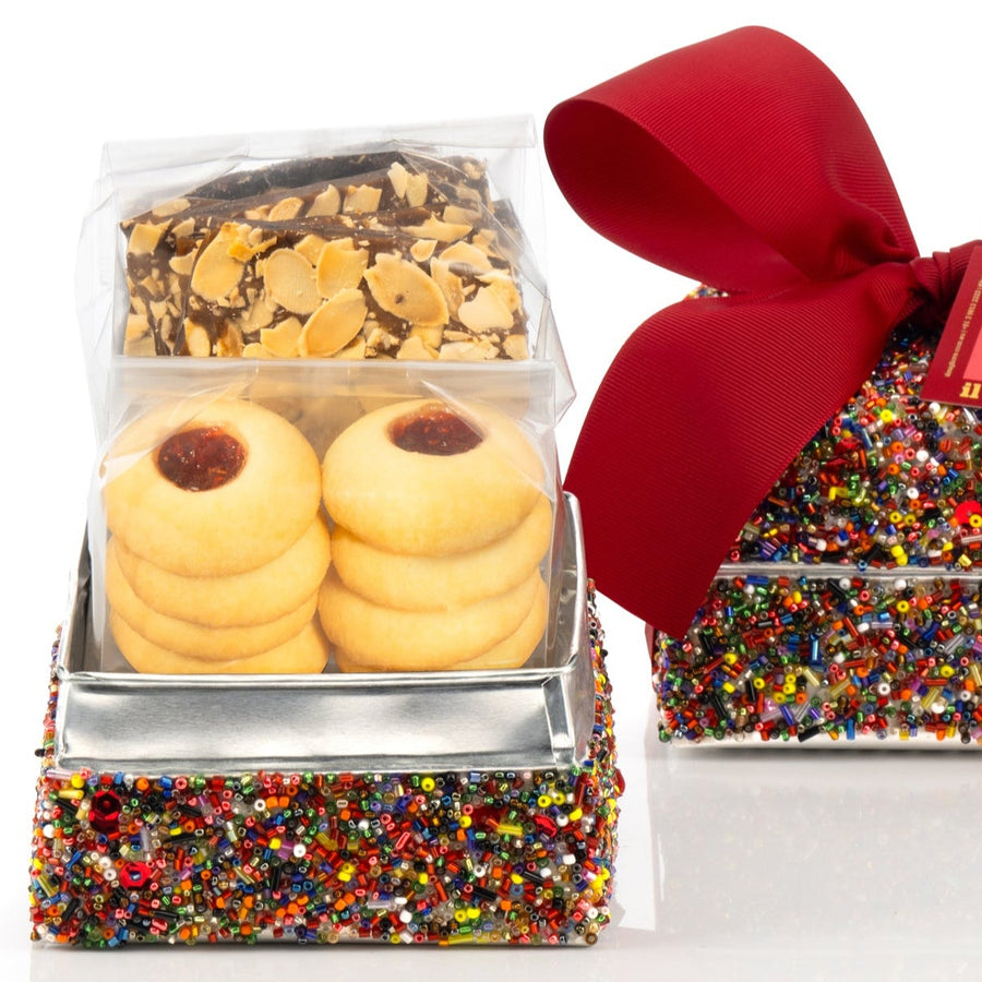 Decorative sequin box with delicious biscuits and a red ribbon on a white background