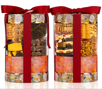 Two cylindrical gift boxes with red ribbons filled with assorted snacks on a white background