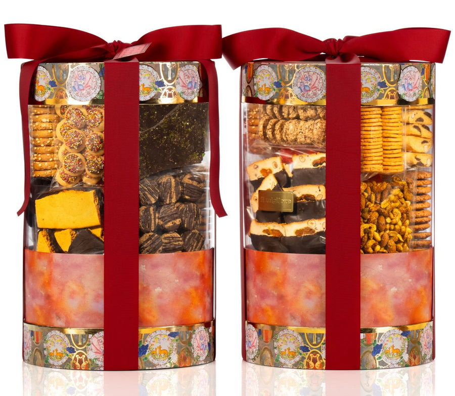 Two cylindrical gift boxes with red ribbons filled with assorted snacks on a white background